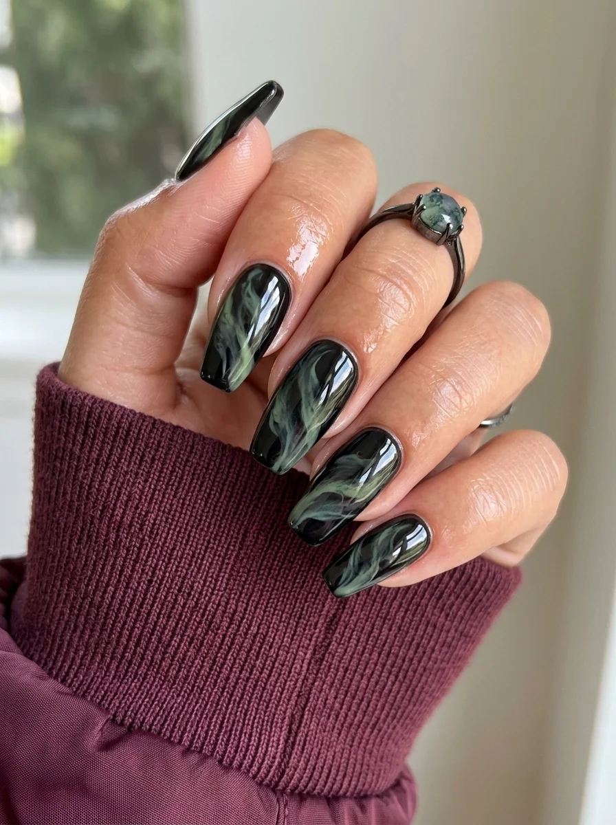 Long coffin nails with a black base and smoky green marble swirl effect.