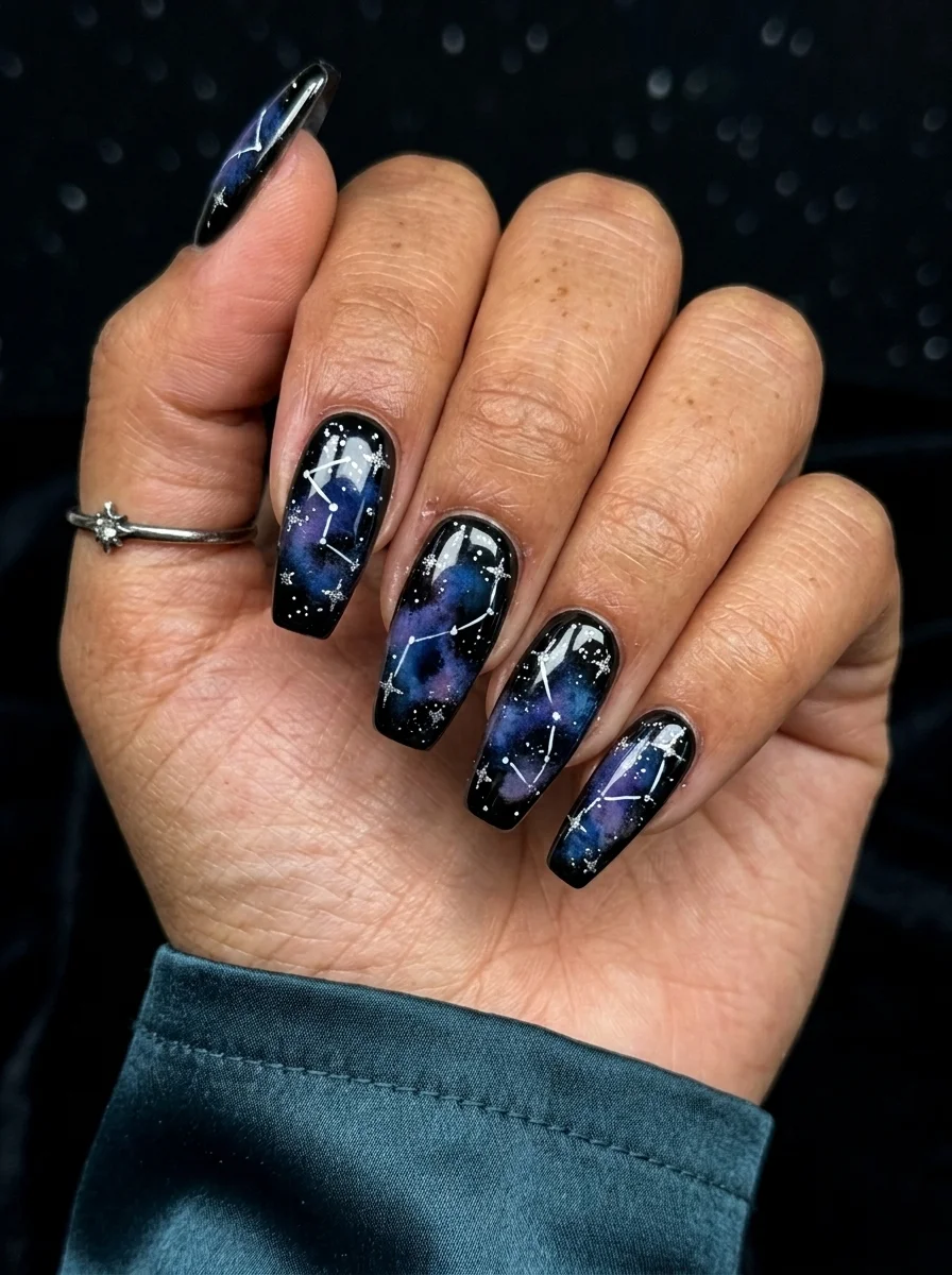 Long almond nails with a dark navy-to-black gradient base and silver constellation dot patterns.