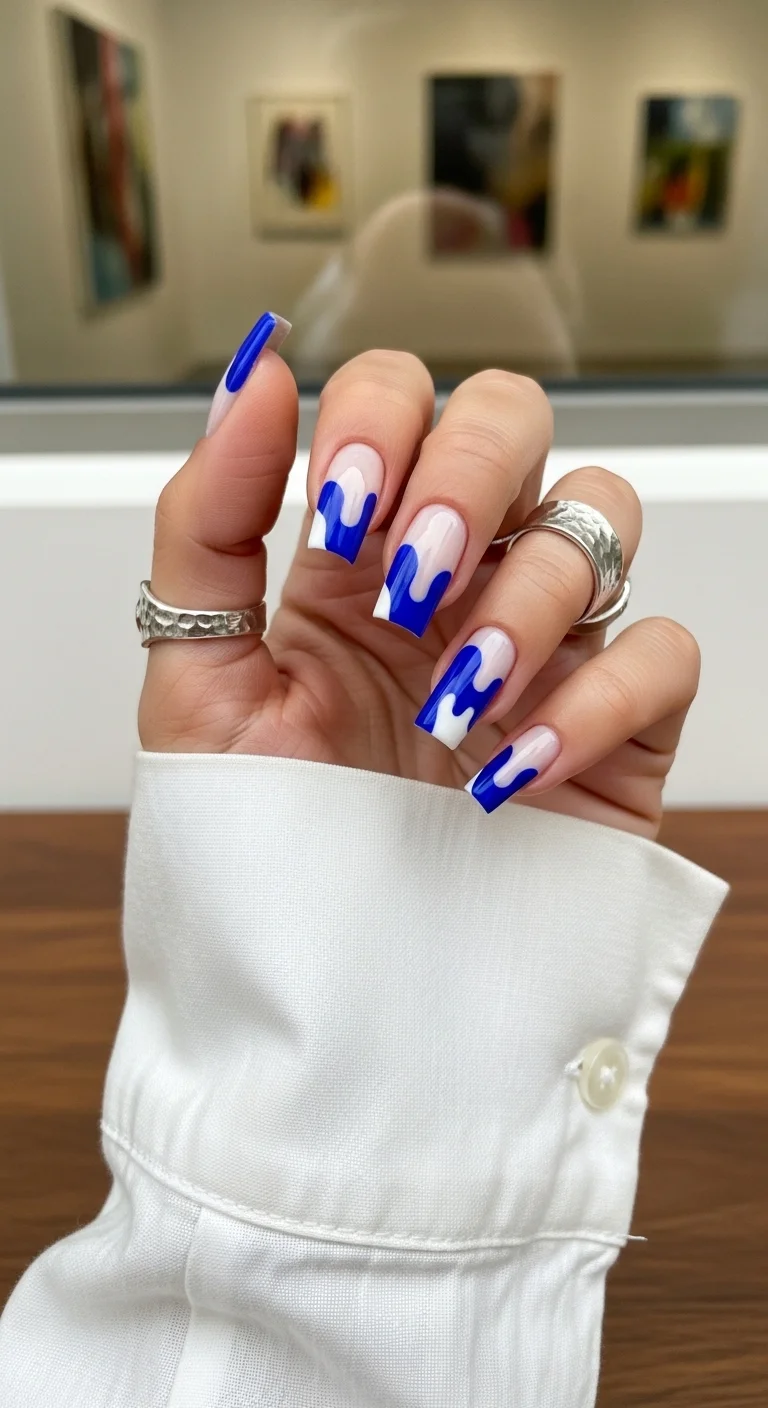 Long square nails with a nude base and electric blue 'drip' style French tips.